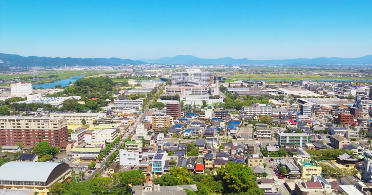 青い空と雲の下、広い川が流れ、手前には緑の土手と散歩道が広がる風景